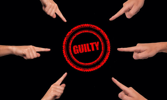 Sechs Zeiger zeigen auf einen roten Kreis, in dessen Mitte auf schwarzem Hintergrund das Wort „GUILTY“ steht.