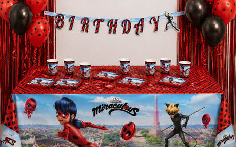 Ein Geburtstagstisch im „Miraculous Ladybug“-Stil mit passenden Tellern, Bechern und einer Tischdecke; ein „BIRTHDAY“-Banner sowie schwarze und rote Luftballons schmücken den Bereich.