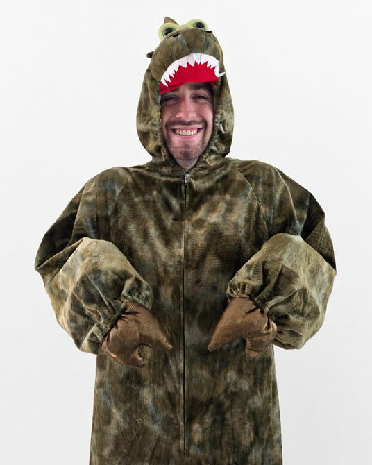 Eine lächelnde Person, die ein flauschiges Dinosaurierkostüm mit Krallenhandschuhen und einer Kapuze mit Augen und Zähnen trägt und vor einem schlichten weißen Hintergrund steht.