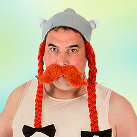 Ein Mann, der einen Helm im Wikinger-Stil, einen großen orangefarbenen Kunstschnurrbart und lange orangefarbene Zöpfe trägt und ein beiges Oberteil mit schwarzen Schleifenverzierungen anhat.