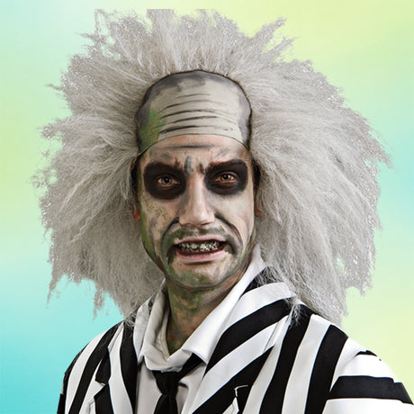Eine Person in einem schwarz-weiß gestreiften Anzug mit zerzaustem weißem Haar, bemaltem Gesicht mit dunklen Ringen um die Augen und grünlichem Make-up, die vor einem Hintergrund mit Farbverlauf steht.