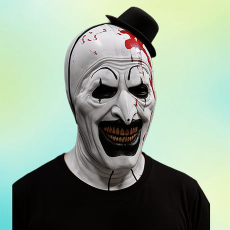 Eine Person, die eine gruselige weiße Clownmaske mit schwarzen Akzenten trägt, mit Kunstblut am Kopf, einem kleinen schwarzen Hut und einem schwarzen Hemd, vor einem Hintergrund mit Farbverlauf.