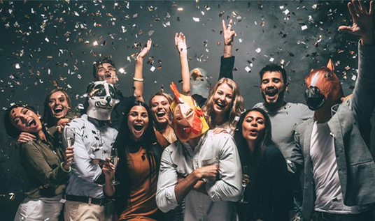 Eine Gruppe von Menschen feiert auf einer Party mit Konfetti; einige tragen Tiermasken, alle wirken fröhlich und ausgelassen.