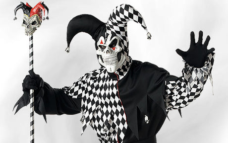 Eine Person in einem schwarz-weißen Harlekin-Kostüm mit Totenkopfmaske und Narrenkappe, die einen dazu passenden Stab in der Hand hält und mit erhobener Hand posiert.
