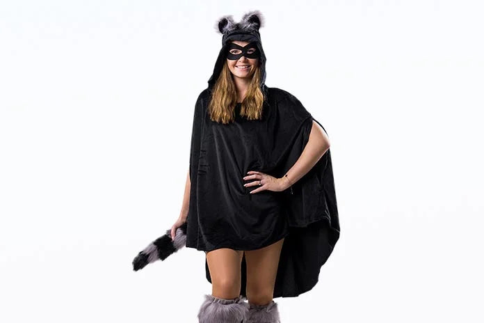 Eine Frau in einem schwarzen Waschbärenkostüm mit Ohren, Maske, gestreiftem Schwanz und pelzigen Stulpen, die vor einem schlichten weißen Hintergrund steht.