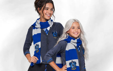 Zwei Personen, die passende blaue und graue Schals, Strickjacken und Krawatten mit einem Wappen tragen, stehen nebeneinander und lächeln vor einem schlichten Hintergrund.