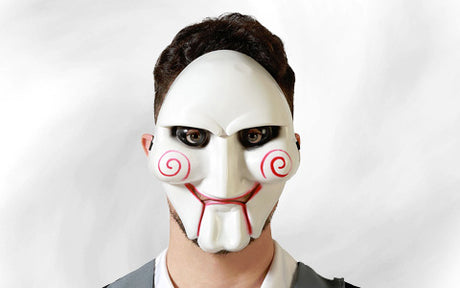 Eine Person, die eine weiße Maske mit roten, spiralförmigen Wangen, markanten Wangenknochen und schwarzem Augen-Make-up trägt und vor einem schlichten, hellen Hintergrund steht.