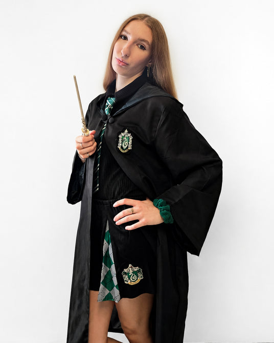 Eine Person, die eine Slytherin-Robe trägt und einen Zauberstab in der Hand hält, gekleidet in einem schwarz-grünen Outfit im Harry-Potter-Stil vor einem schlichten weißen Hintergrund.