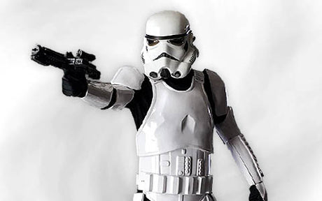Eine Person, die ein weißes Sturmtruppen-Kostüm aus „Star Wars“ trägt, hält einen Blaster in der Hand und richtet ihn vor einem schlichten Hintergrund nach vorne.