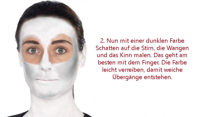Person mit weißer Gesichtsbemalung und dunklen Schattierungen um Augen, Wangen und Kinn; ein deutscher Text erklärt, wie man die Schattierungen mit dem Finger aufträgt, um sanfte Übergänge zu erzielen.