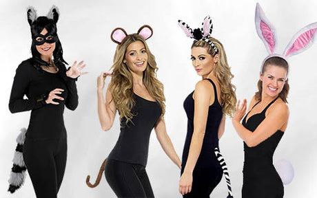 Vier Frauen in schwarzen Outfits mit Tieraccessoires: ein Waschbär, eine Maus, ein Zebra und ein Kaninchen, die jeweils die entsprechenden Ohren und Schwänze tragen und vor einem weißen Hintergrund in einer Reihe stehen.