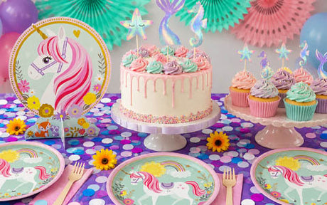 Ein Geburtstagstisch im Einhorn-Stil mit einer Torte, Cupcakes, Einhorn-Tellern, bunten Dekorationen und pastellfarbenen Luftballons.