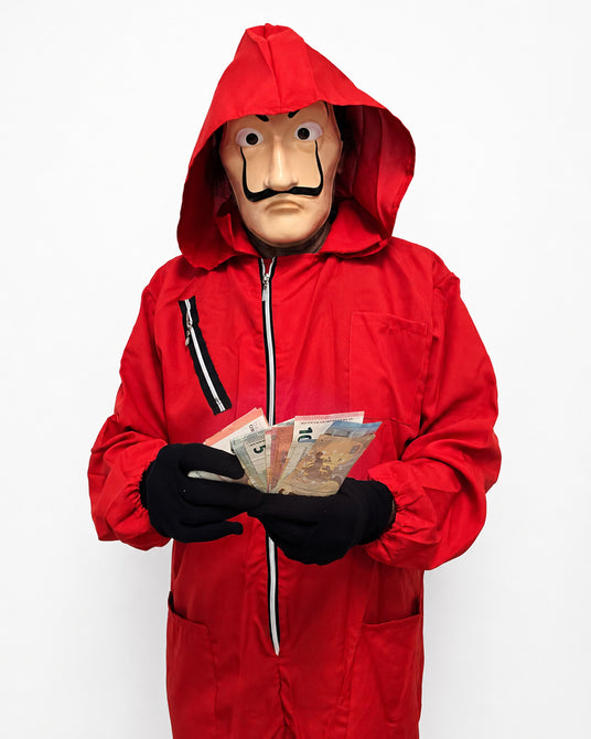Eine Person in einem roten Overall mit Kapuze und einer Maske, die mehrere Banknoten in der Hand hält und vor einem schlichten weißen Hintergrund steht.