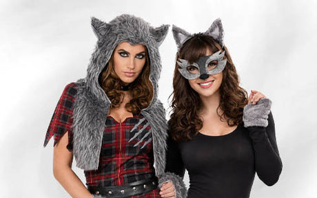 Zwei Frauen in Wolfs- und Katzenkostümen stehen nebeneinander; die eine trägt eine Kapuze aus Kunstfell und ein kariertes Kleid, die andere ein Stirnband mit Katzenohren, eine Maske und Handschuhe in Pfotenform.
