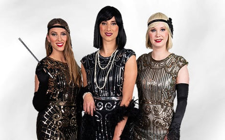 Drei Frauen in Flapper-Kleidern und mit Accessoires im Stil der 1920er Jahre posieren gemeinsam vor einem schlichten weißen Hintergrund.