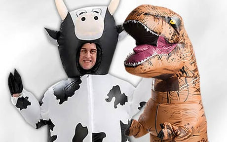 Zwei Personen tragen aufblasbare Kostüme, eine ist als schwarz-weiße Kuh verkleidet, die andere als brauner Dinosaurier mit offenem Maul.