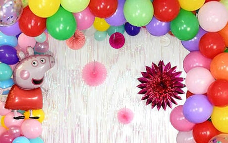 Ein bunter Ballonbogen und ein Peppa-Pig-Ballon auf der linken Seite vor einem weißen Hintergrund mit rosa Papierdekorationen sorgen für eine festliche Partystimmung.