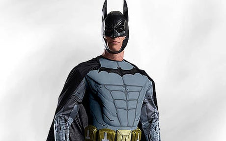 Eine Person in einem Batman-Kostüm steht vor einem schlichten weißen Hintergrund und trägt einen schwarzen Umhang, eine Maske und einen Werkzeuggürtel.