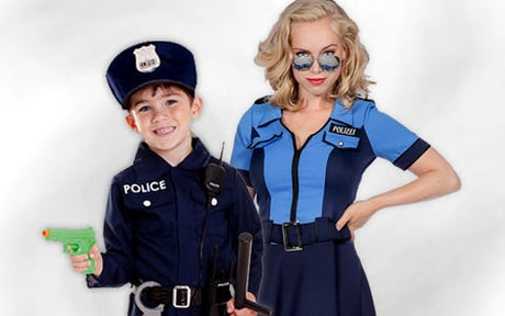 Ein Kind und eine erwachsene Person in Polizeikostümen stehen nebeneinander; das Kind hält eine grüne Spielzeugpistole und einen Schlagstock in der Hand, während die erwachsene Person eine Sonnenbrille trägt und eine Hand in die Hüfte gestützt hat.
