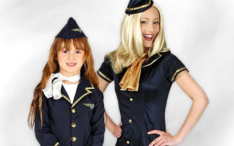 Ein junges Mädchen und eine erwachsene Frau tragen identische marineblaue Flugbegleiterinnen-Uniformen mit Mützen und goldenen Akzenten und posieren vor einem einfarbigen Hintergrund.