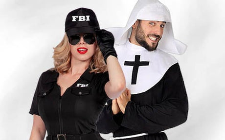 Eine Frau in einem FBI-Kostüm und ein Mann in einem Nonnenkostüm stehen nebeneinander und lächeln beide vor einem schlichten weißen Hintergrund in die Kamera.