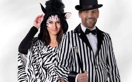 Zwei Erwachsene in Kostümen mit Zebra-Motiv: Der eine ist als Zebra verkleidet, mit Gesichtsbemalung und Ohren, der andere trägt einen schwarz-weiß gestreiften Anzug und einen Zylinder; beide stehen gemeinsam vor einem einfarbigen Hintergrund.