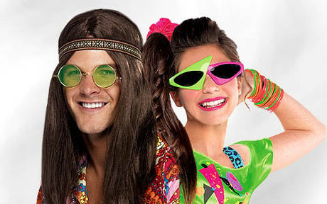 Zwei Personen in bunten Retro-Kostümen mit auffälligen Accessoires wie Sonnenbrillen und Schmuck posieren und lächeln vor einem schlichten Hintergrund.