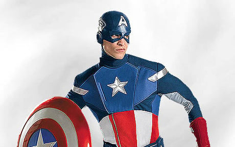 Eine als Captain America verkleidete Person steht da und hält ein rot-weiß-blaues Schild in der Hand; sie trägt ein passendes Superheldenkostüm mit einem Stern-Emblem und einem „A“ auf dem Helm.