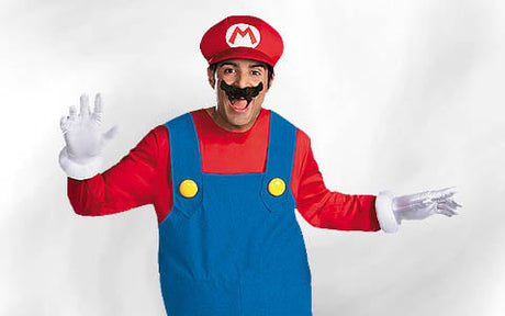 Eine Person mit einem roten Hut mit einem „M“, einem roten Hemd, einer blauen Latzhose, weißen Handschuhen und einem schwarzen falschem Schnurrbart, die mit erhobenen Händen posiert.