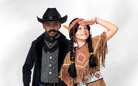Ein Kind in einem Cowboy-Kostüm steht neben einem Kind in einem von den amerikanischen Ureinwohnern inspirierten Kostüm vor einem schlichten weißen Hintergrund.