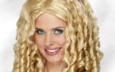 Eine Frau mit langen, stark gelockten blonden Haaren und strahlend blauen Augen, die vor einem schlichten, hellen Hintergrund in die Kamera lächelt.