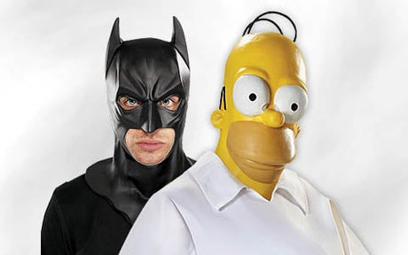 Zwei Personen posieren in Kostümen vor einem schlichten weißen Hintergrund: Die eine ist als Batman in schwarzer Maske und schwarzem Anzug verkleidet, die andere als Homer Simpson mit gelber Maske und weißem Hemd.