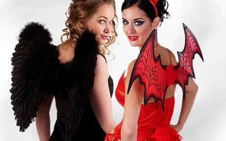 Zwei Frauen stehen Rücken an Rücken; die eine trägt schwarze Engelsflügel und ein schwarzes Kleid, die andere rote Teufelsflügel und ein rotes Outfit.