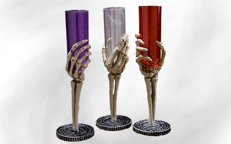 Drei Plastikbecher mit Stielen in Form von Skeletthänden, von denen jeder einen violetten, durchsichtigen oder roten Becher enthält, vor einem schlichten weißen Hintergrund.