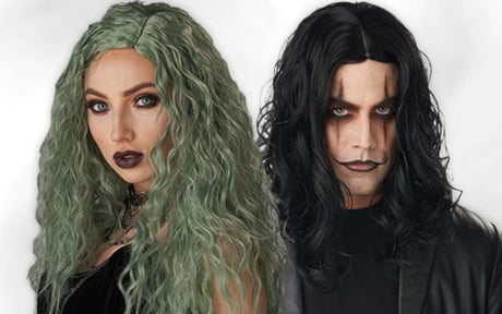 Zwei Personen mit langen, welligen Haaren, eine mit grünen Haaren und dunklem Make-up, die andere mit schwarzen Haaren und auffälliger Gesichtsbemalung; beide tragen dunkle Kleidung vor einem schlichten Hintergrund.