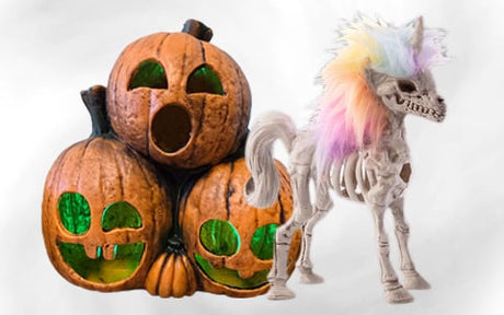 Drei geschnitzte Kürbisse mit grünen Lichtern sind neben einem Einhornskelett mit einer regenbogenfarbenen Mähne vor einem weißen Hintergrund aufgestapelt.