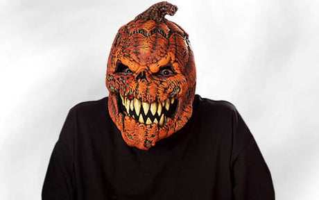 Eine Person, die eine detailreiche, gruselige Kürbismaske mit scharfen Zähnen und einem wütenden Gesichtsausdruck trägt, gekleidet in ein schlichtes schwarzes T-Shirt vor einem weißen Hintergrund.