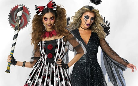 Zwei Frauen in Halloween-Kostümen: Die eine trägt ein gestreiftes, mit Blutspritzern übersätes Kleid und hält eine Requisitensäge in der Hand, die andere ein schwarzes Kleid mit Flügeln; beide sind auffällig geschminkt.