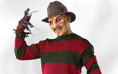 Eine Person in einem rot-grün gestreiften Pullover und einer braunen Mütze, die einen Handschuh mit Metallklauen trägt und Make-up aufweist, das wie Narben im Gesicht aussieht, posiert mit erhobener Hand vor einem weißen Hintergrund.
