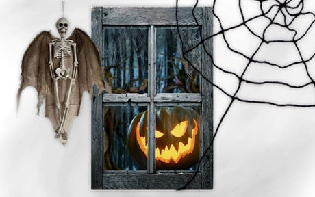 Ein hängendes Fledermausskelett, ein Fenster mit einer leuchtenden Kürbislaterne und ein großes schwarzes Spinnennetz auf weißem Hintergrund.