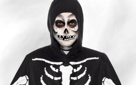 Eine Person in einem Skelettkostüm mit Kapuze und Totenkopf-Gesichtsbemalung, die vor einem einfarbigen Hintergrund direkt in die Kamera blickt.