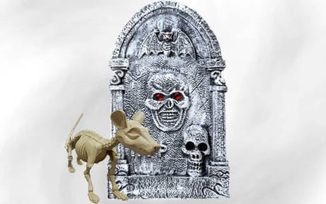 Ein Skelettmodell einer Maus steht vor einem grauen Grabstein, der mit Totenkopf- und Fledermausmotiven verziert ist; der Haupttotenkopf hat rote Augen.