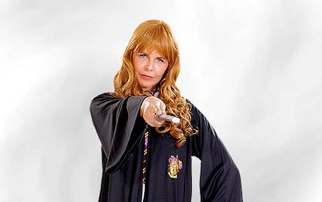 Eine Person in einer schwarzen Robe mit Wappen, die einen Zauberstab in der Hand hält und damit nach vorne zeigt, vor einem schlichten weißen Hintergrund.