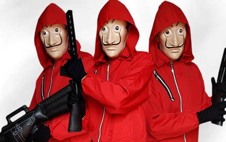 Drei Personen in roten Overalls mit Kapuze und Salvador-Dalí-Masken halten schwarze Spielzeugpistolen vor einem schlichten weißen Hintergrund in die Kamera.