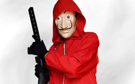 Eine Person in einer roten Kapuzenjacke trägt eine Maske im Stil von Salvador Dalí und hält vor einem schlichten weißen Hintergrund eine schwarze Schusswaffe in der Hand.