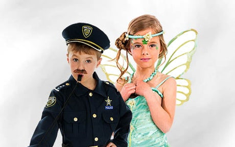 Ein Kind in einem Polizistenkostüm steht neben einem anderen Kind, das als Fee mit Flügeln verkleidet ist; beide posieren für ein Foto.