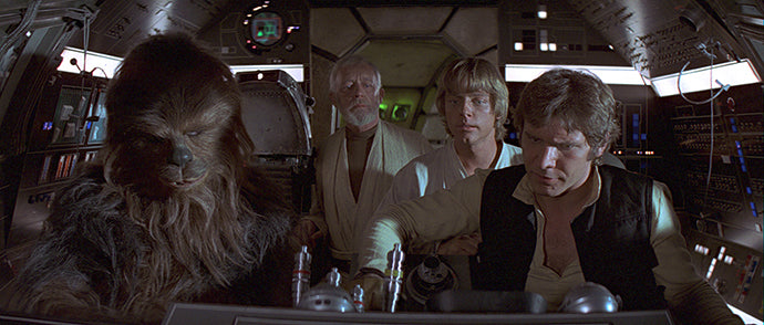 Vier Figuren, darunter eine große, pelzige Gestalt, sitzen im Cockpit eines Raumschiffs, umgeben von Bedienfeldern, und blicken mit ernsten Mienen nach vorne.