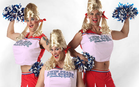 Drei Erwachsene, gekleidet wie Cheerleader in einheitlichen Uniformen der Twin Peaks High School, mit blonden Perücken und blauen und weißen Pompons in den Händen, posieren voller Energie vor einem weißen Hintergrund.