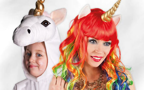 Ein Kind in einem weißen Einhornkostüm steht neben einem Erwachsenen, der eine Regenbogenperücke und ein Stirnband mit Einhornhorn trägt.