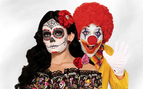 Eine Person mit „Tag der Toten“-Make-up und -Kostüm steht neben einer Person, die als Clown verkleidet ist – mit roter Perücke, weißen Handschuhen und einem bunten Outfit – und winkt in die Kamera.